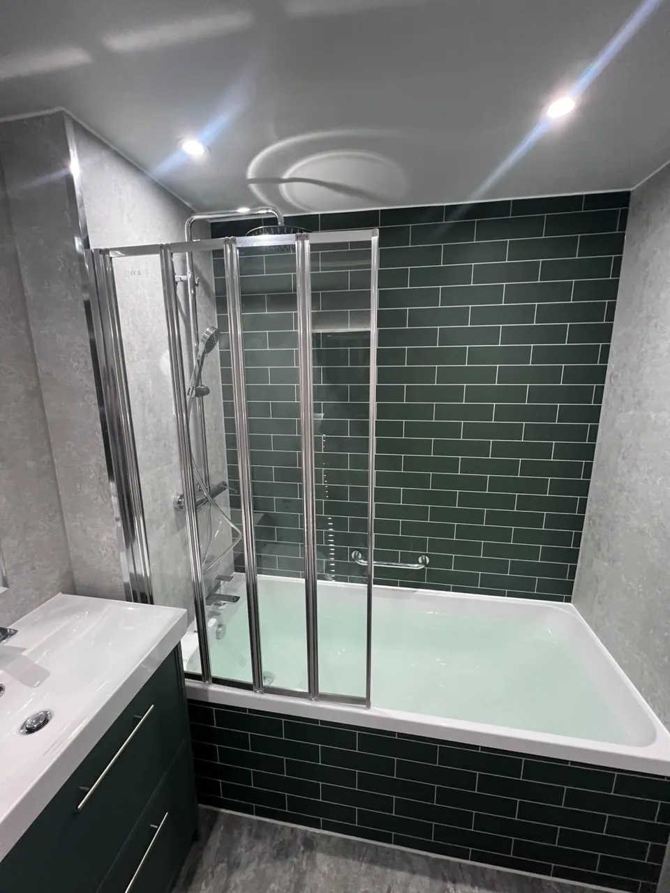 Green-tiled bath with shower screen and fitted storage